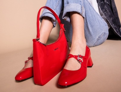 Rote Lackleder-Mary Janes an Damenfüßen. Dazwischen steht die dazu passende Handtasche aus rotem Lackleder, beides aus der &quot;Classy in Paris&quot;-Kollektion von HUMANIC