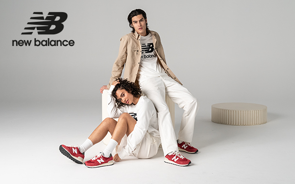 Ein Mann und eine Frau mit hellen Outfits und roten Sneakers von New Balance